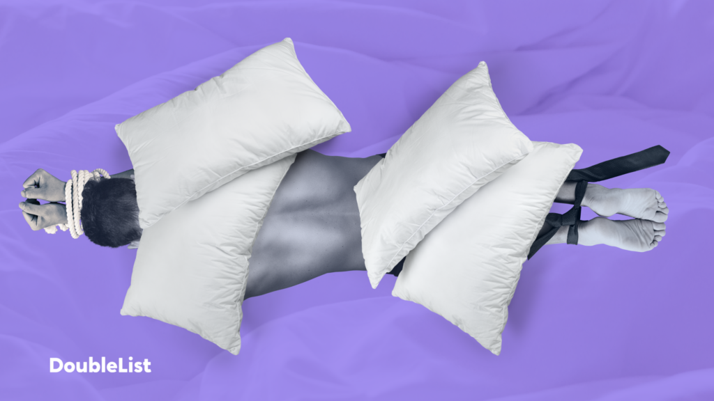 DoubleList graphic of a shirtless man facedown under four pillows with his feet and hands bound in front of a purple backdrop.