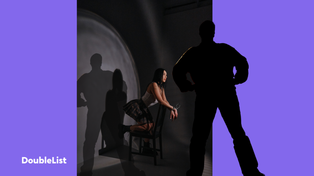 DoubleList graphic of a shadowy man in front of a woman in a dark room with handcuffs in between purple backdrop panels.